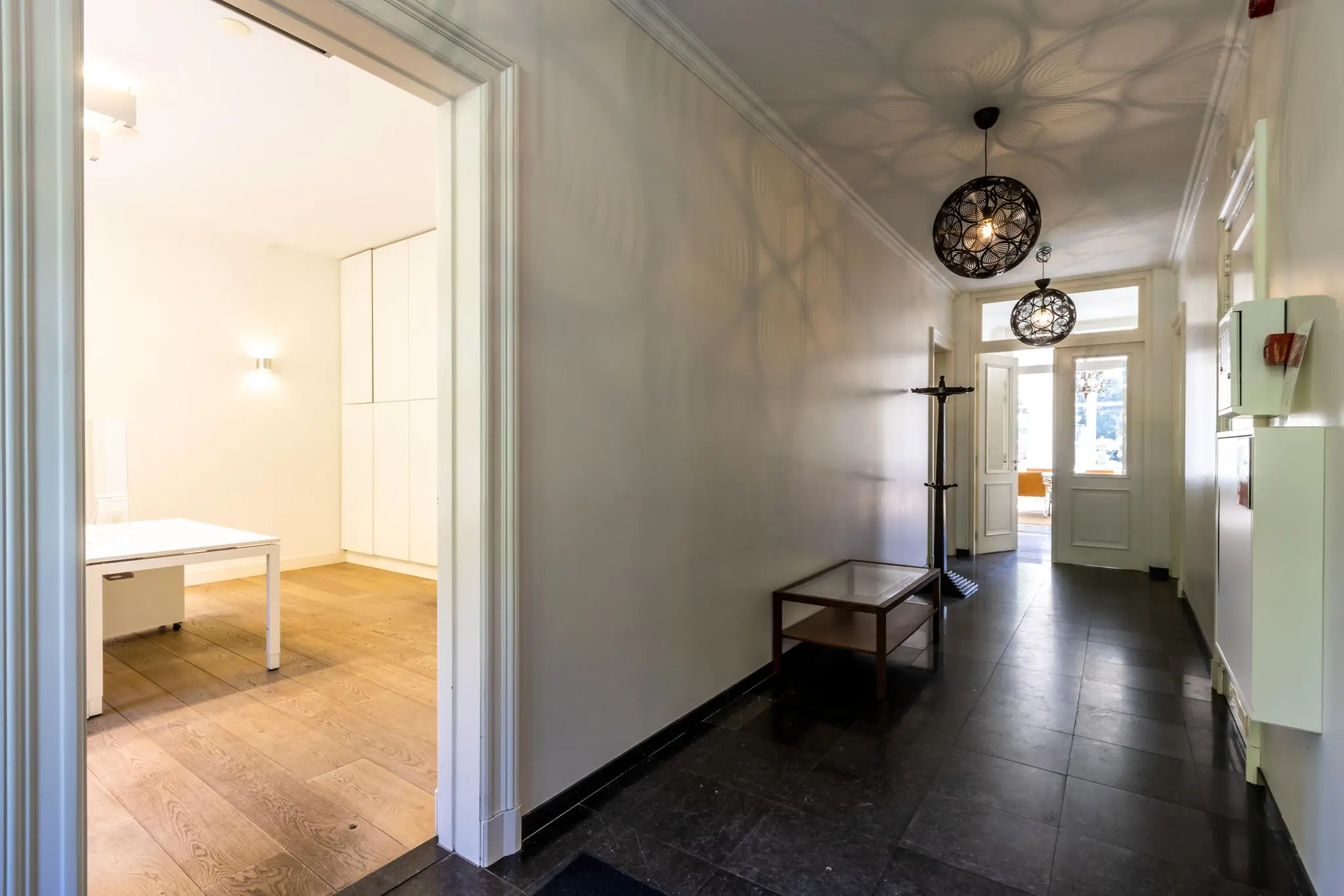 Lichte hal met zwarte vloertegels, moderne hanglampen en zicht op een kantoorruimte en buitendeur aan de Langbroekerdijk A.